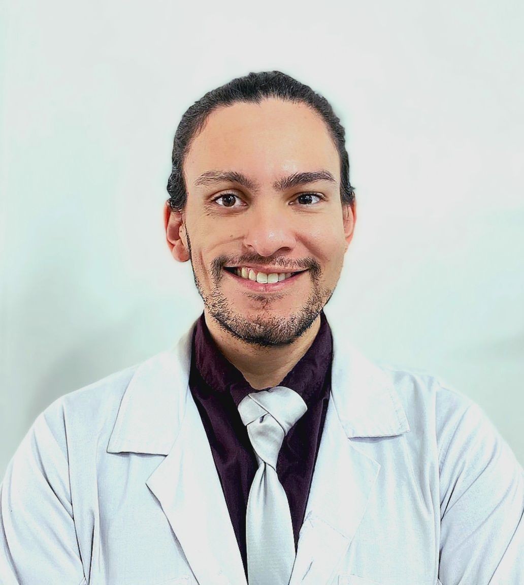 Smiling man in a white lab coat and tie, with a light background.
