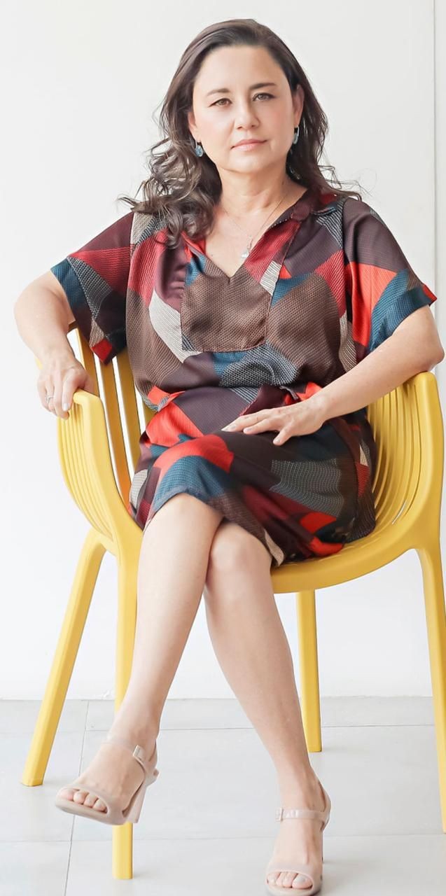 Woman in a colorful dress sitting confidently on a yellow chair against a white background.